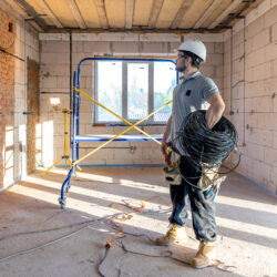 An electrician examines a construction drawing while holding an electrical cable in his hand at a work site.