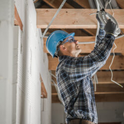 Caucasian Professional Electrician in His 40s Installing Ceiling Light Point Inside Newly Developed Concrete Brick House with Wooden Beams Roof Structure.